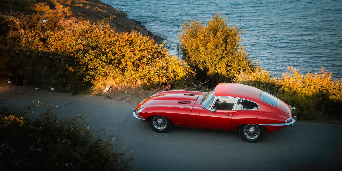 Une voiture ancienne arrêtée sur une route en corniche au-dessus de la mer